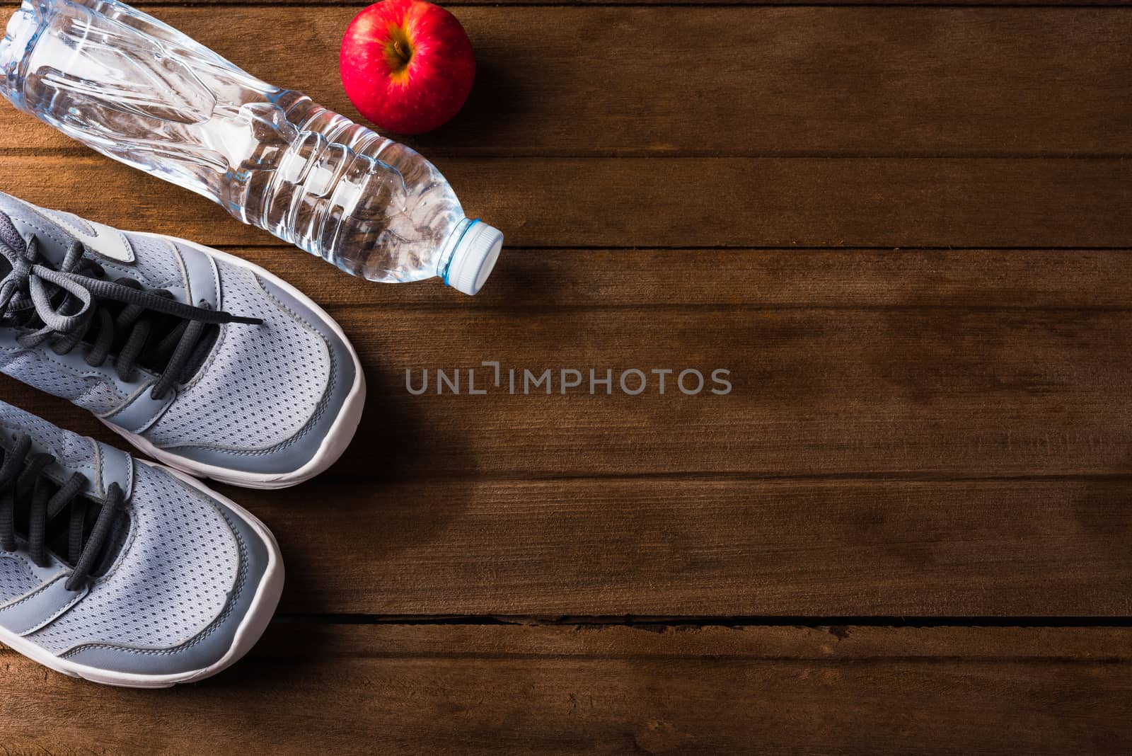 Top view of pair sports shoes, bottle water and red apple on wood table, Gray sneakers and accessories equipment in fitness GYM, Healthy workout concept