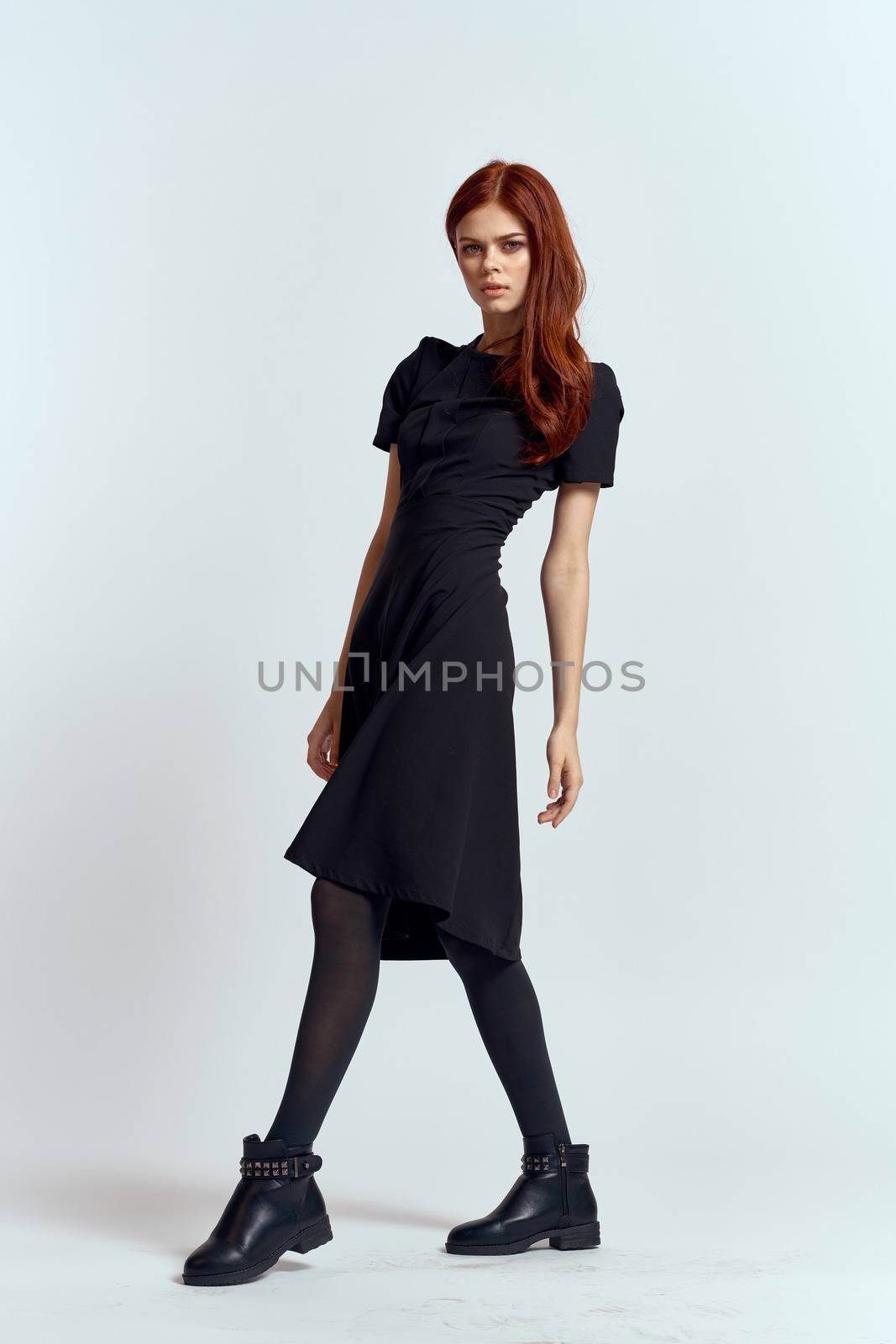 A woman in a black dress on a light background and pantyhose shoes red hair and pose in full growth by SHOTPRIME