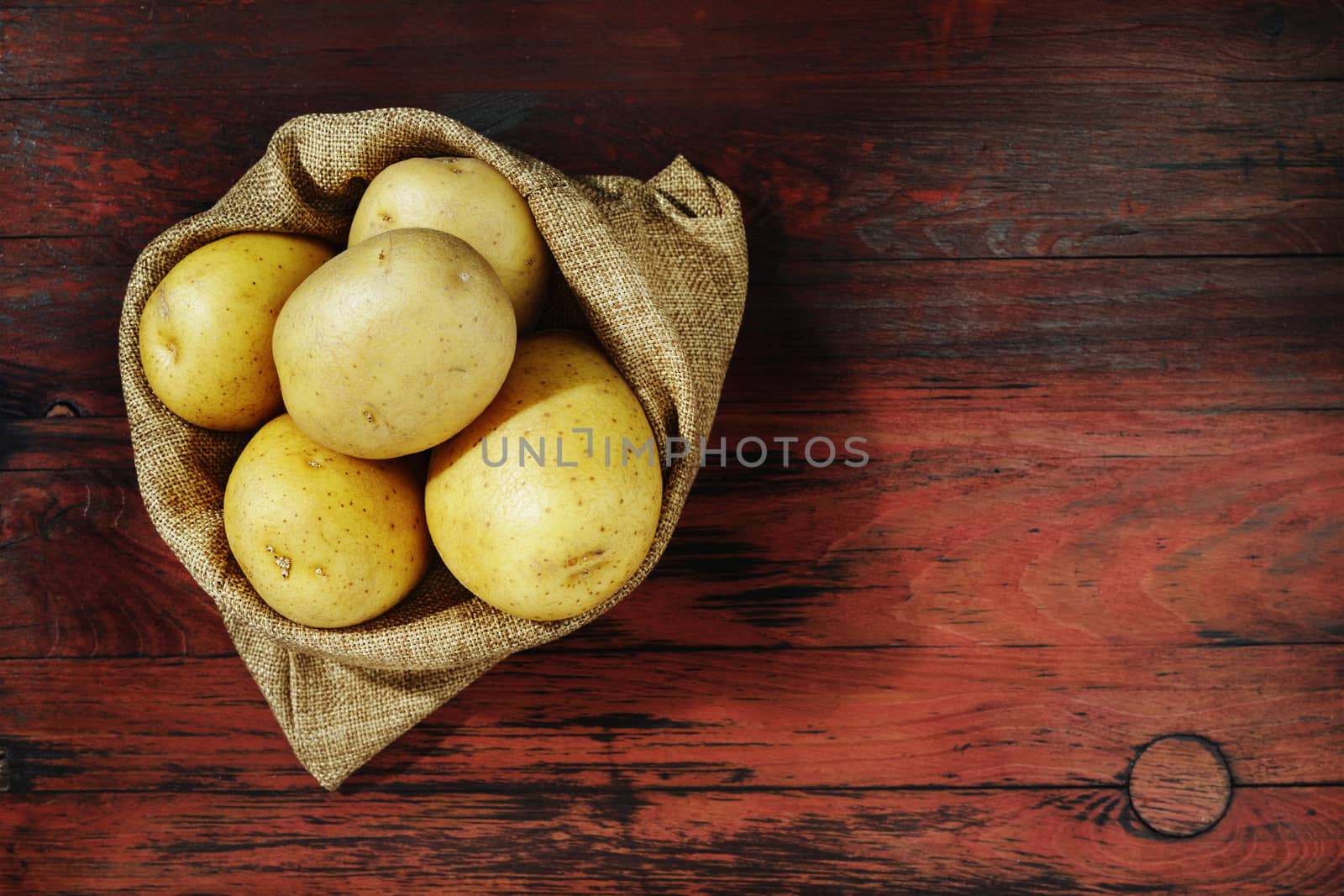 Whole yellow potatoes in bag on red wooden table , uncooked and unpeeled vegetable