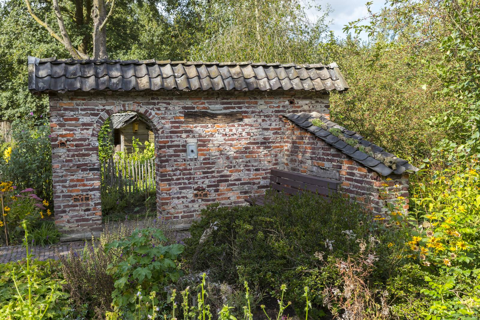 ruin of an old stone shed with an arch as entrance surrounded by plants and flowers in a large green garden