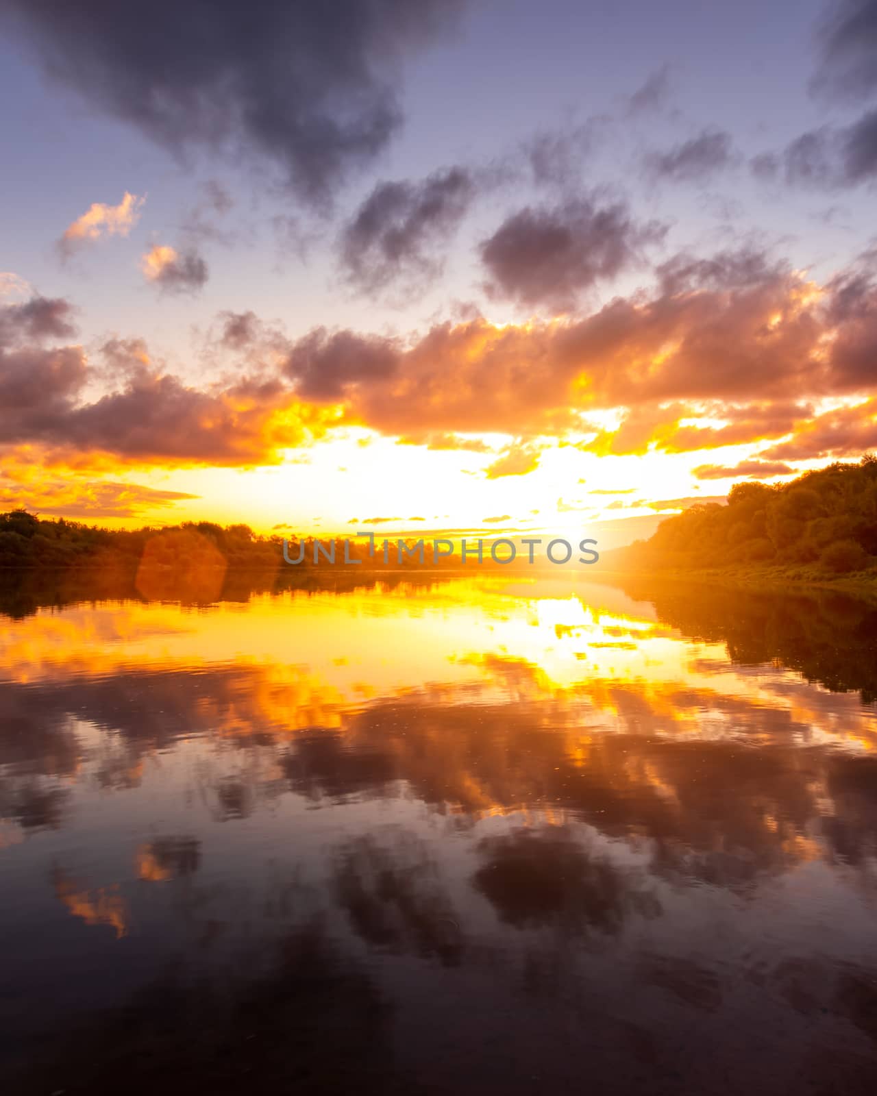 A sunset or sunrise scene over a lake or river with dramatic cloudy skies reflecting in the water on a summer evening or morning. Landscape.