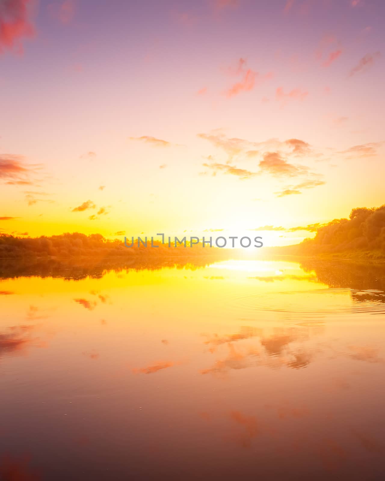 A sunset or sunrise scene over a lake or river with dramatic cloudy skies reflecting in the water on a summer evening or morning. Landscape.