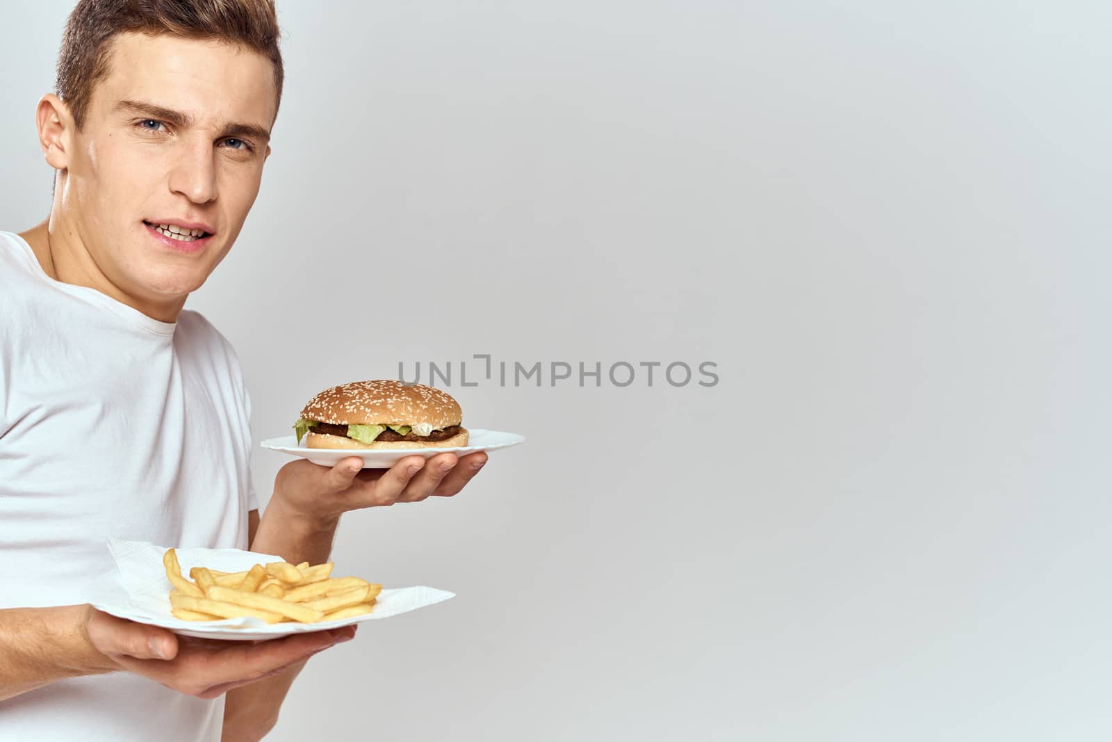 a man with fries and a hamburger on a light background in white t-shirt close-up cropped view Copy Space Model. High quality photo