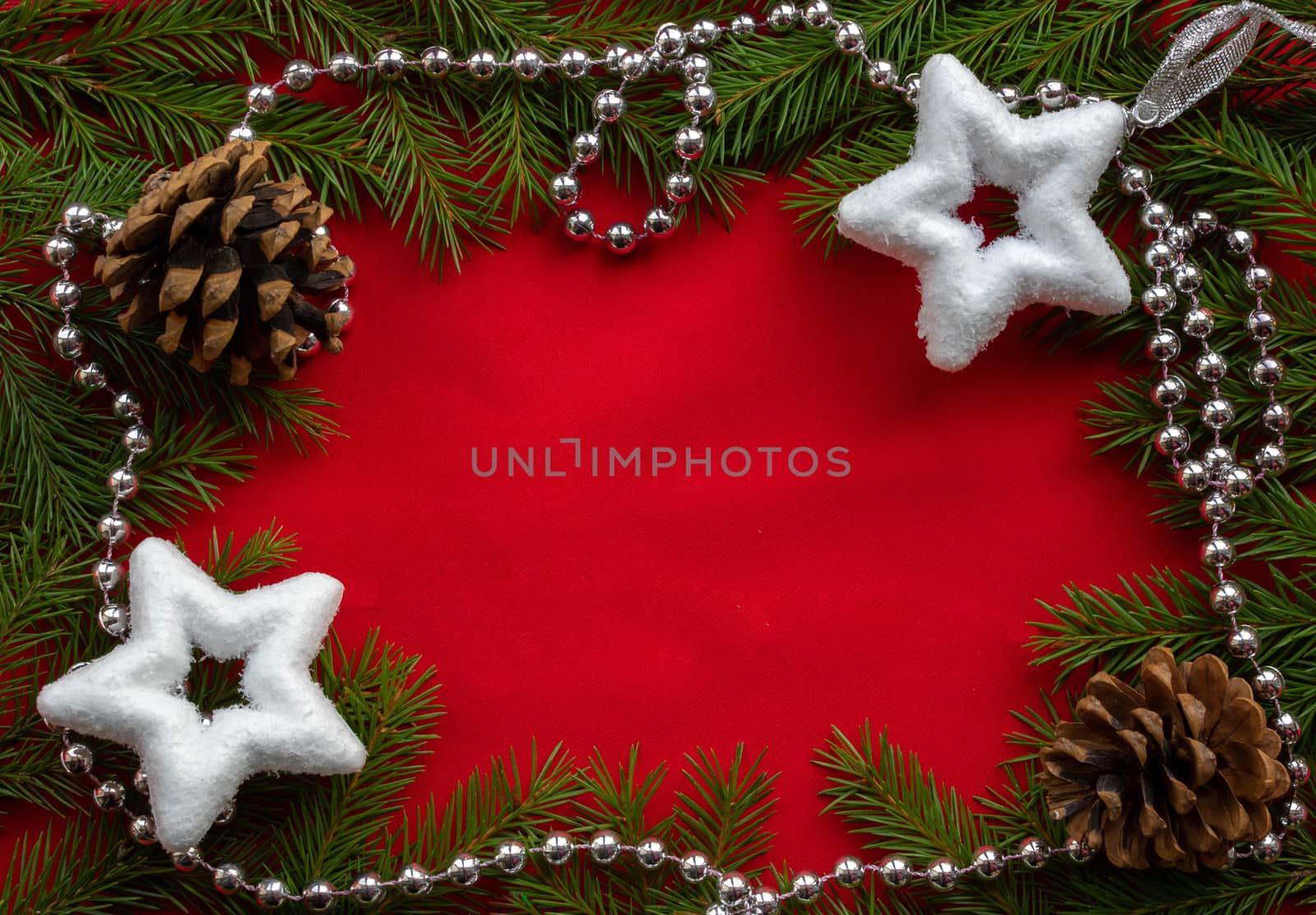 A frame of green fir branches ,two white stars and two cones with silver beads on a red background. The concept of Christmas and New year. Space for your text.