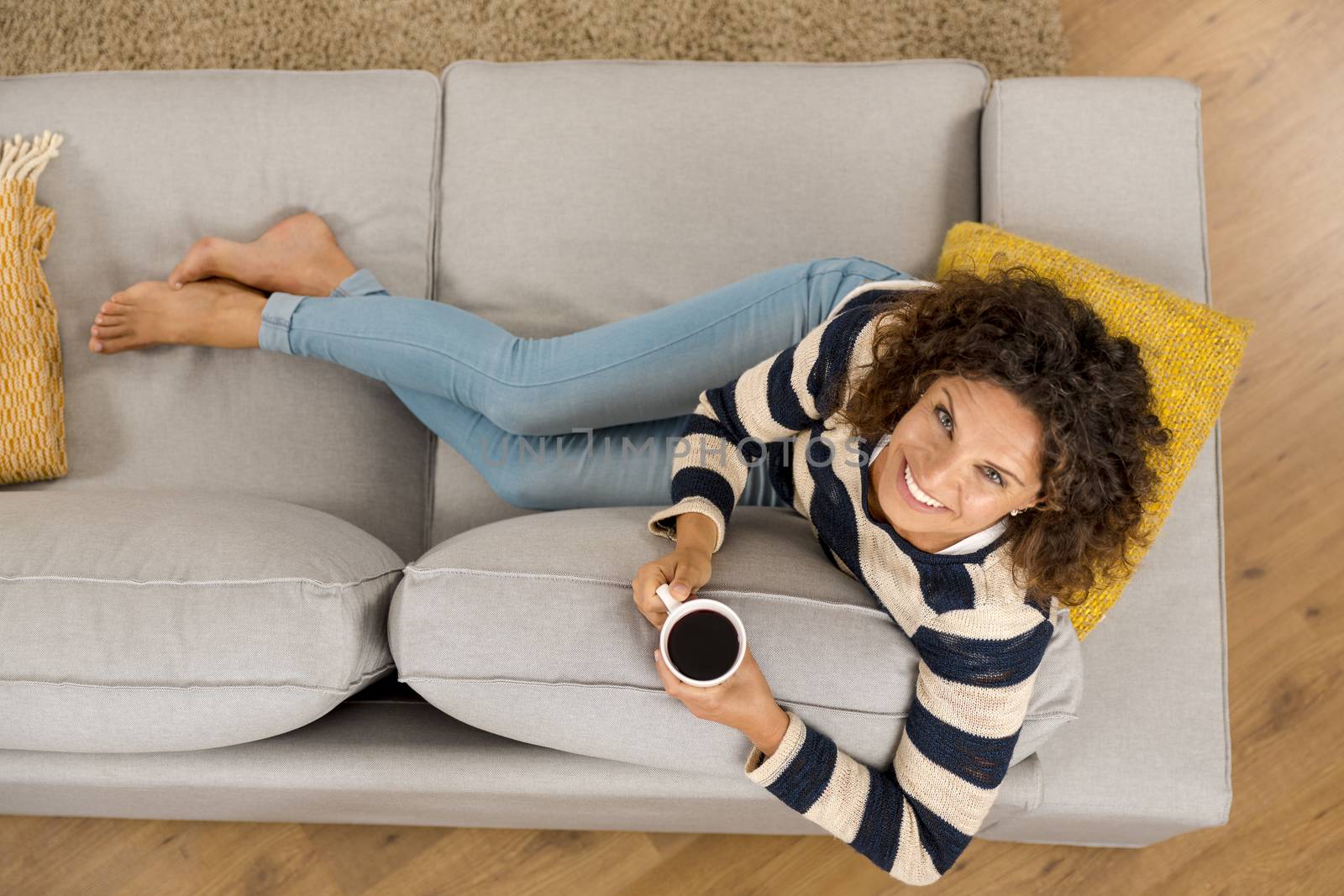 Top view of a beautiful woman on the sofa and drinking coffee