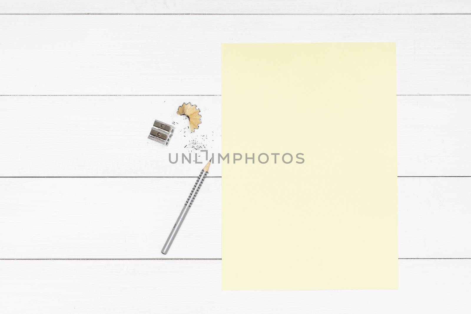 a pencil, a pencil sharpener and a yellow sheet of paper on a white wooden table