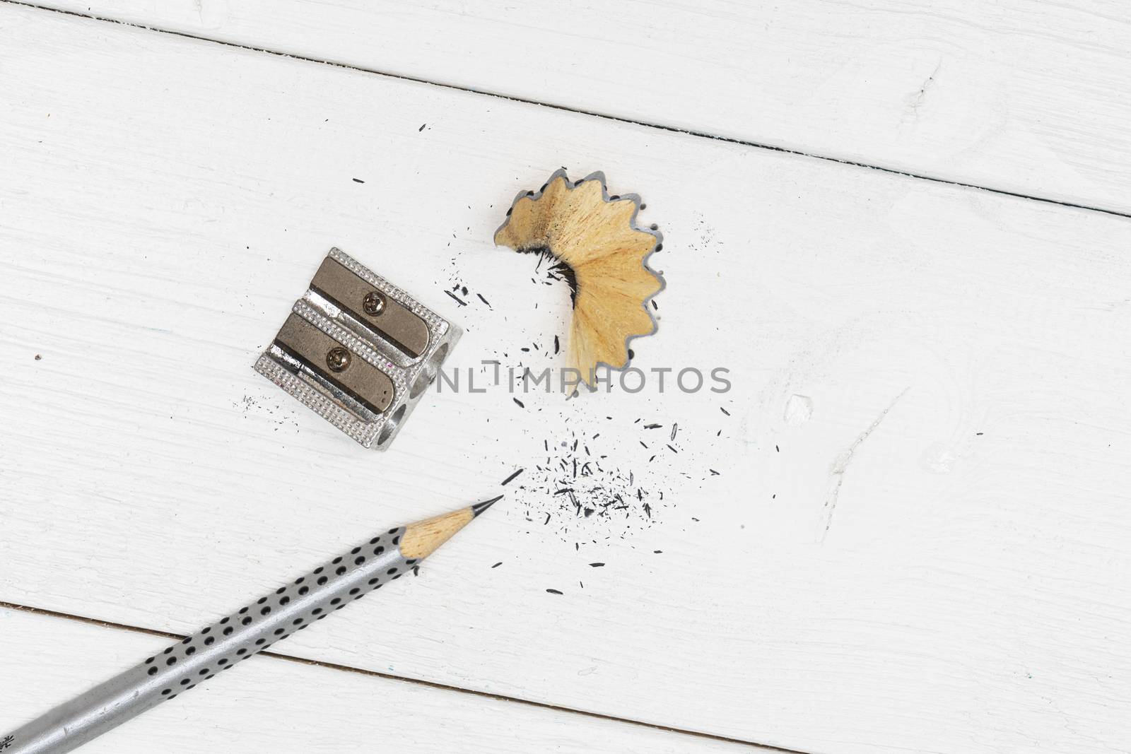 a pencil, a pencil sharpener and some shavings on a white wooden table