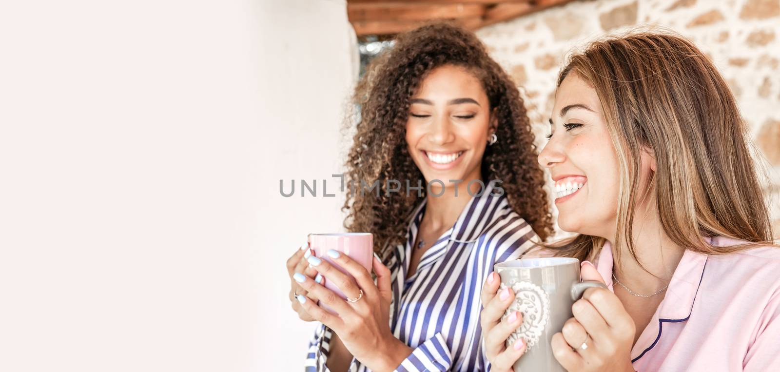 Multi-ethnic best friends women in pajama smiling holding a cup of tea with white copy space to the left - Concept: stay at home and enjoy your life