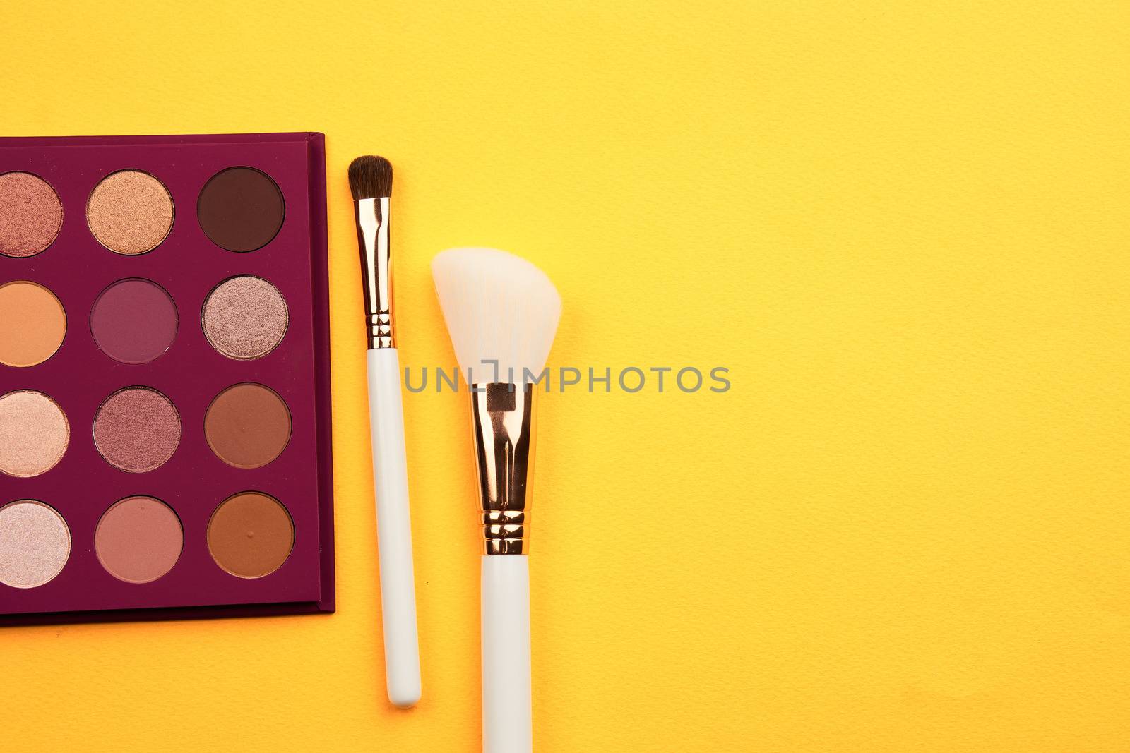 Eyeshadows and makeup brushes on a yellow background top view professional cosmetics by SHOTPRIME