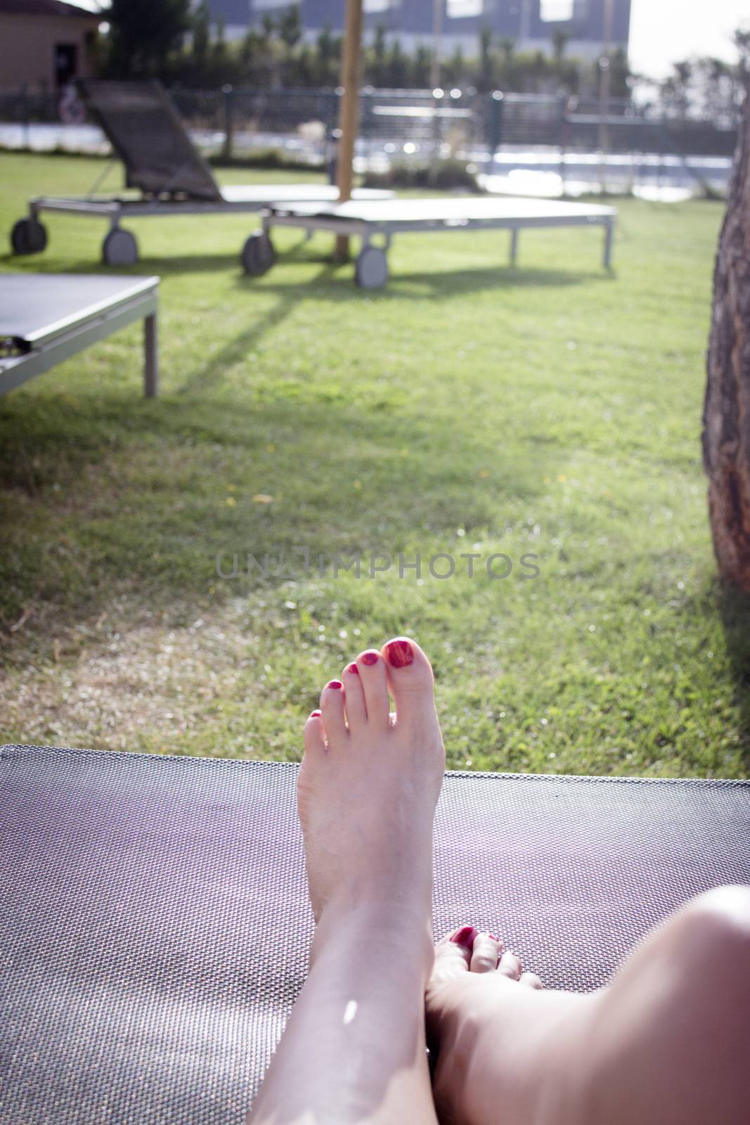 Woman feet on pool lounger sunbathing. Sunny day