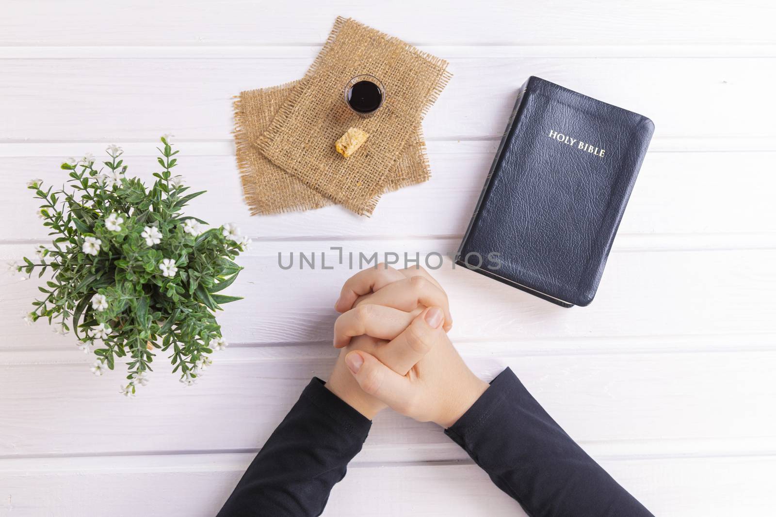 Young woman praying and Taking communion  - the wine and the bread symbols of Jesus Christ blood and body with Holy Bible. Easter Passover and Lord Supper concept Focus on her hands.