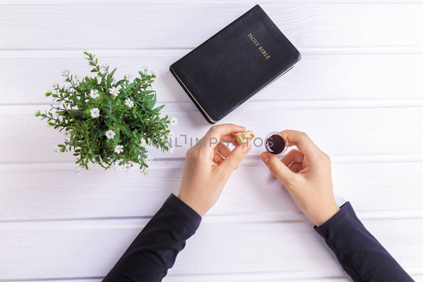 Young woman praying and Taking communion  - the wine and the bread symbols of Jesus Christ blood and body with Holy Bible. Easter Passover and Lord Supper concept Focus on her hands.