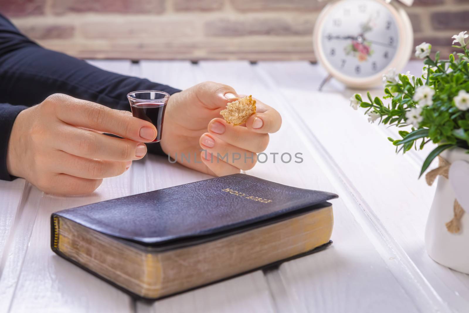 Young woman praying and Taking communion  - the wine and the bread symbols of Jesus Christ blood and body with Holy Bible. Easter Passover and Lord Supper concept Focus on glass.