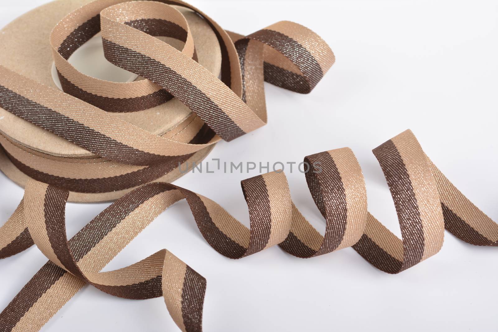 Brown beige Cotton ribbon, roll textilies on bobbin. strapping tape with curl on white backgroud. Use for sewing clothes, bags. Space for text.