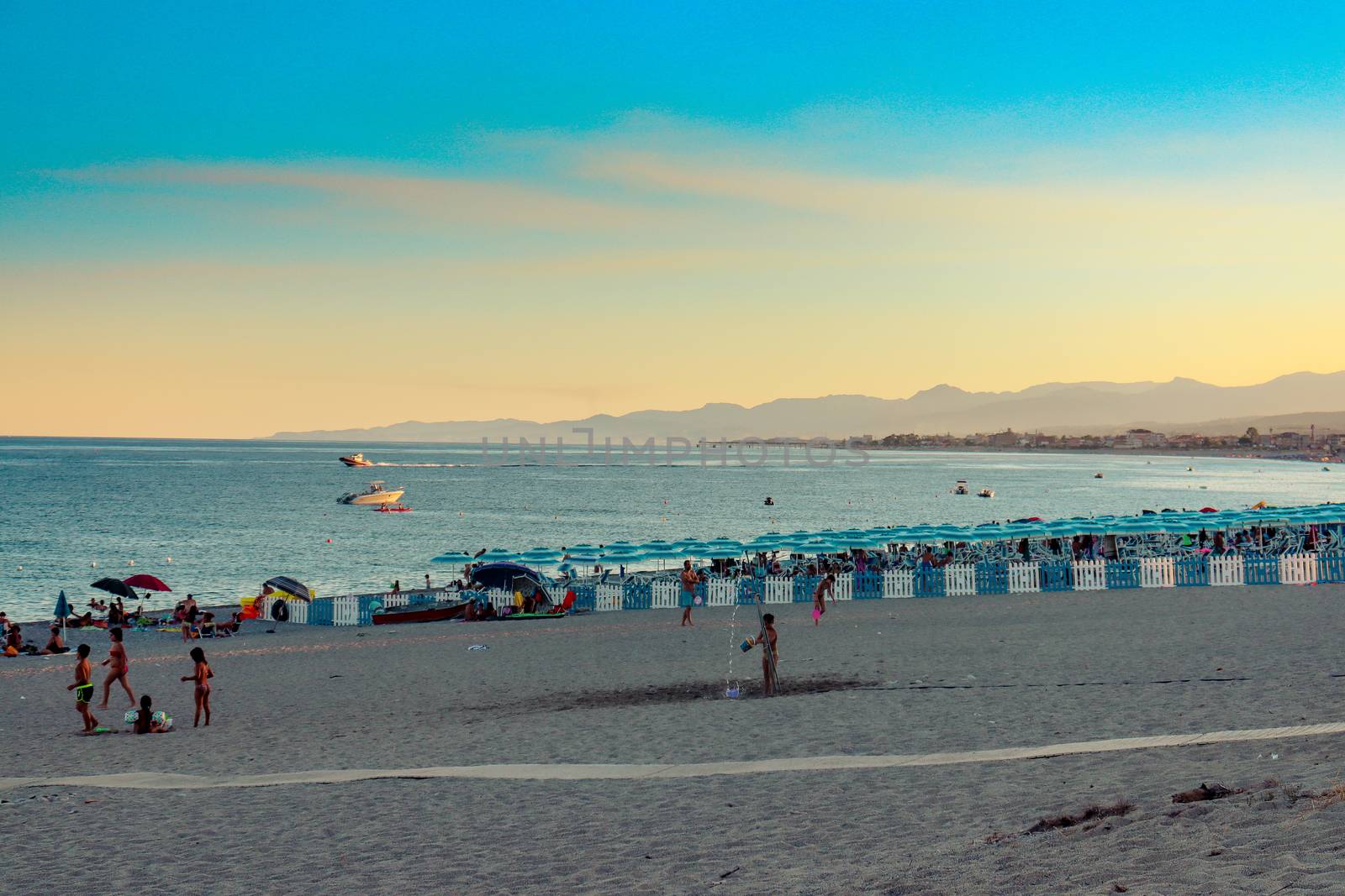 Italian beach with sea and people playing and bathing. Lido on a pebble beach. Blue sky with clear sea by Andreajk3