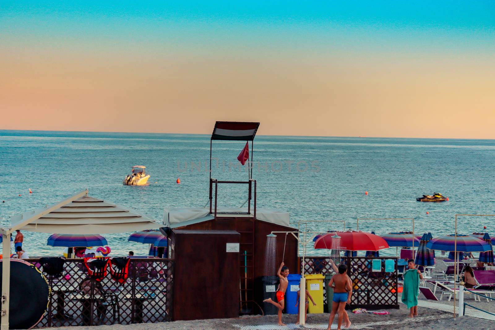 Italian beach with sea and people playing and bathing. Lido on a pebble beach. Blue sky with clear sea by Andreajk3