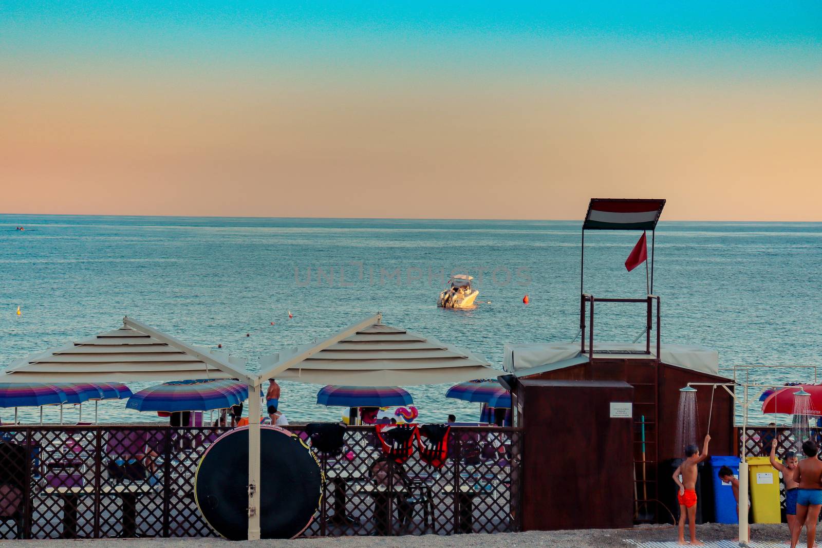 Italian beach with sea and people playing and bathing. Lido on a pebble beach. Blue sky sea