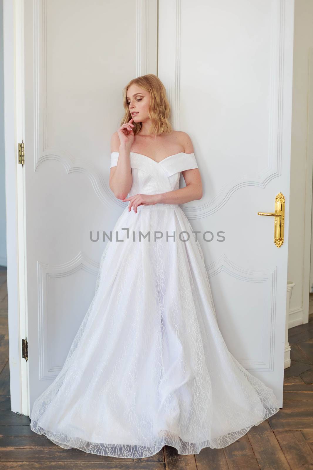 A bride in a chic wedding dress stands near the door and looks to the side thoughtfully