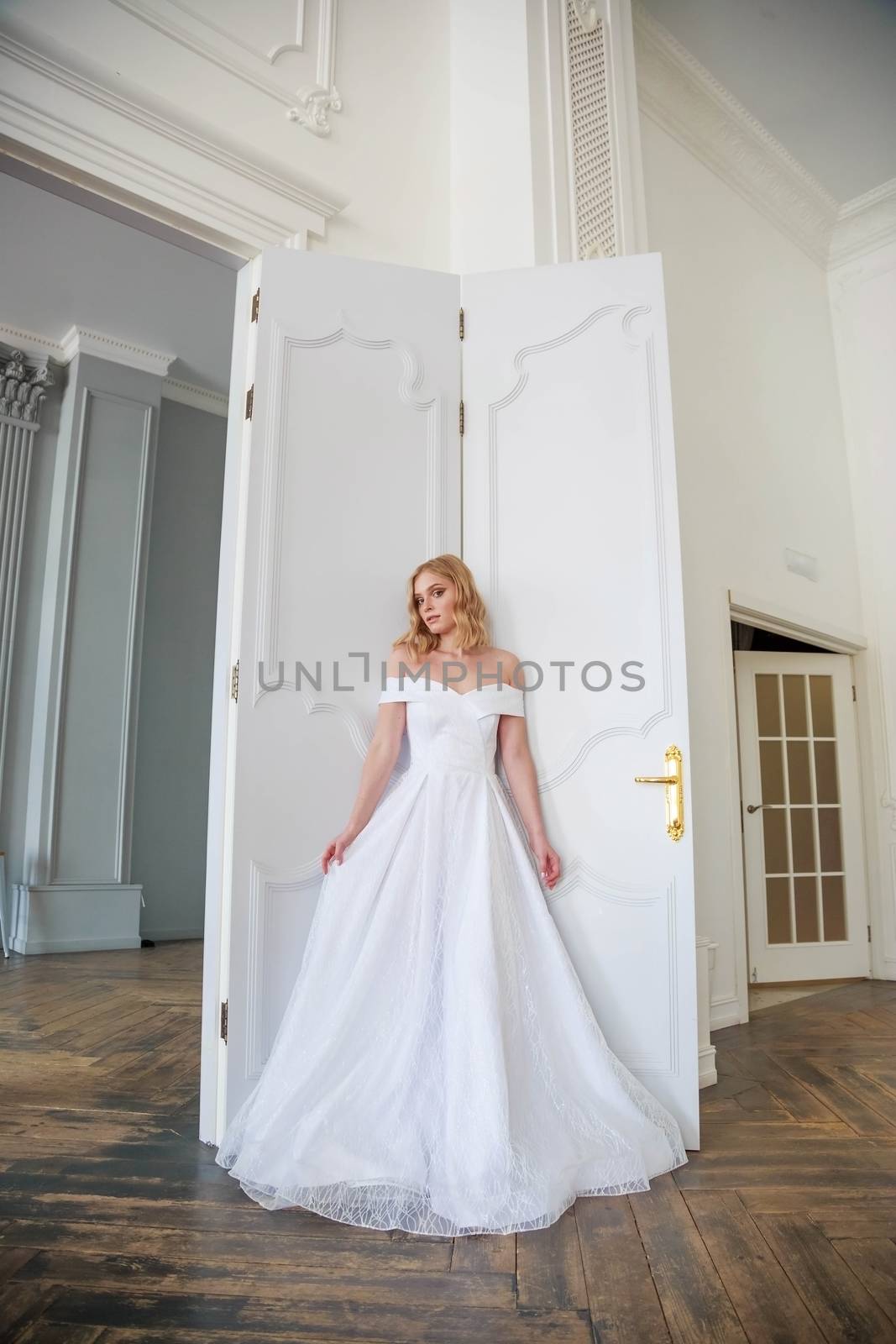 A bride in a chic wedding dress stands near the door and looks to the side by galinasharapova