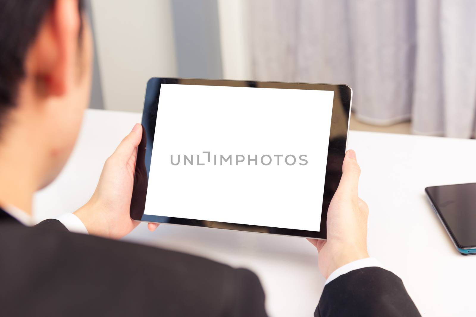 Work from home, Back view of Asian young businessman smile wearing suit video conference call or facetime by smart digital tablet computer blank screen on desk