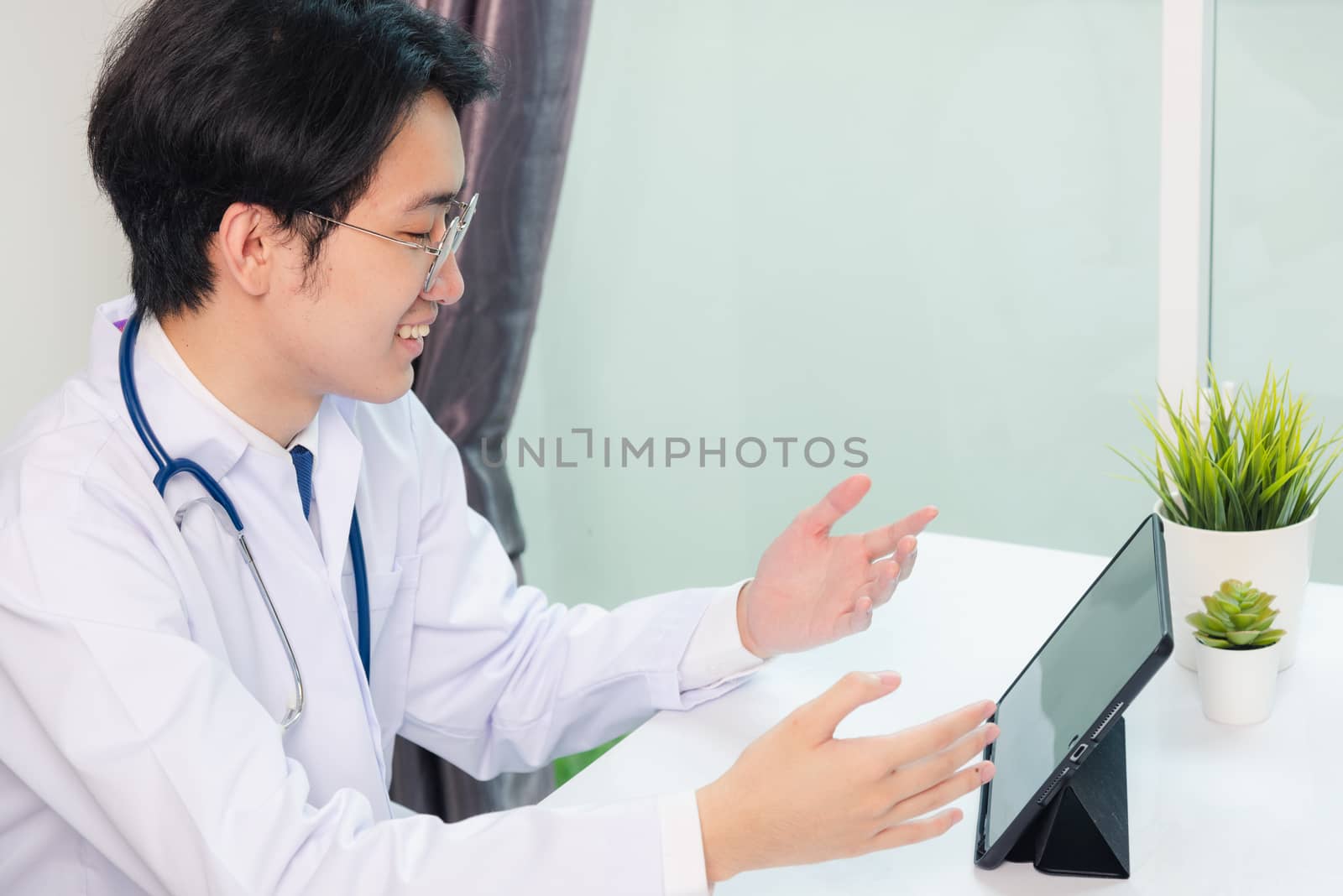 Happy Asian young doctor handsome man smile wear glasses use modern smart digital tablet computer explain patients symptoms of illness on desk at hospital office, Technology Healthcare And Medicine