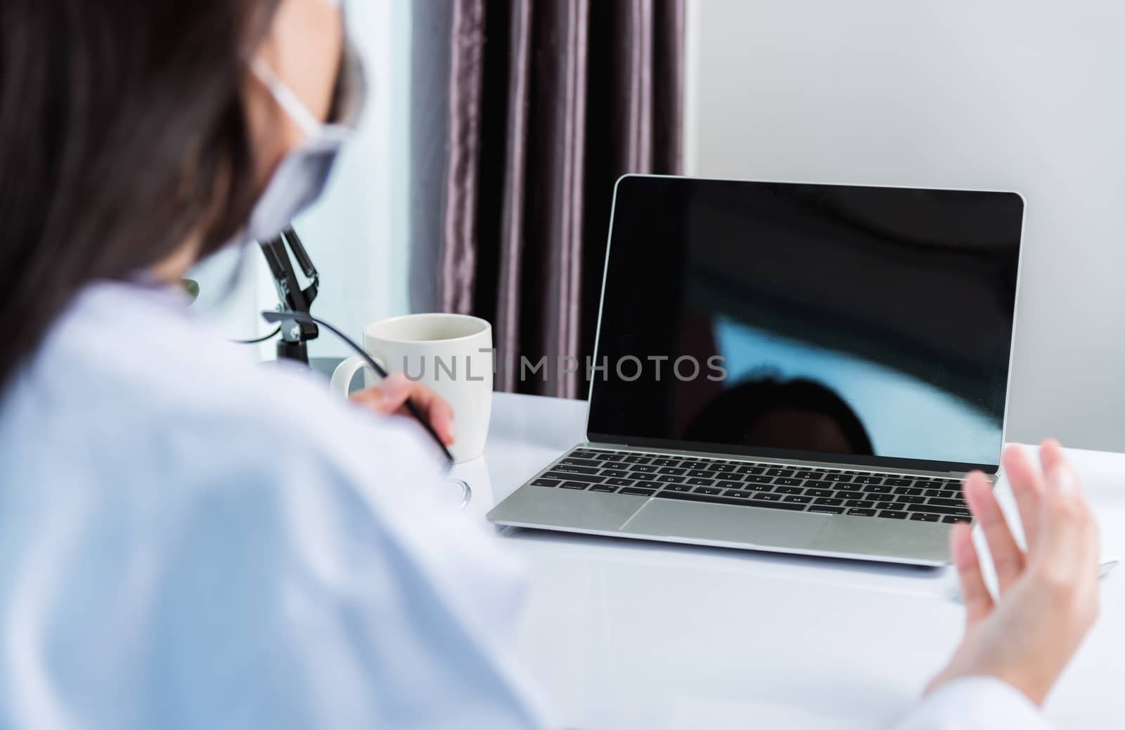 Asian young beautiful woman doctor wear face mask protective video call conference online raise hand explain to patients on laptop computer quarantines disease coronavirus or COVID-19 at hospital