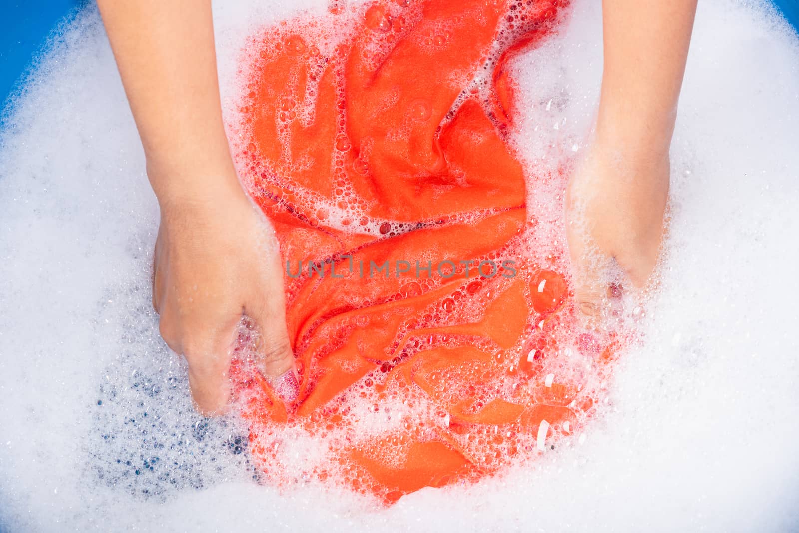 Closeup young Asian woman use hands washing color clothes in basin with detergent have soapy bubble water, studio shot background, laundry concept