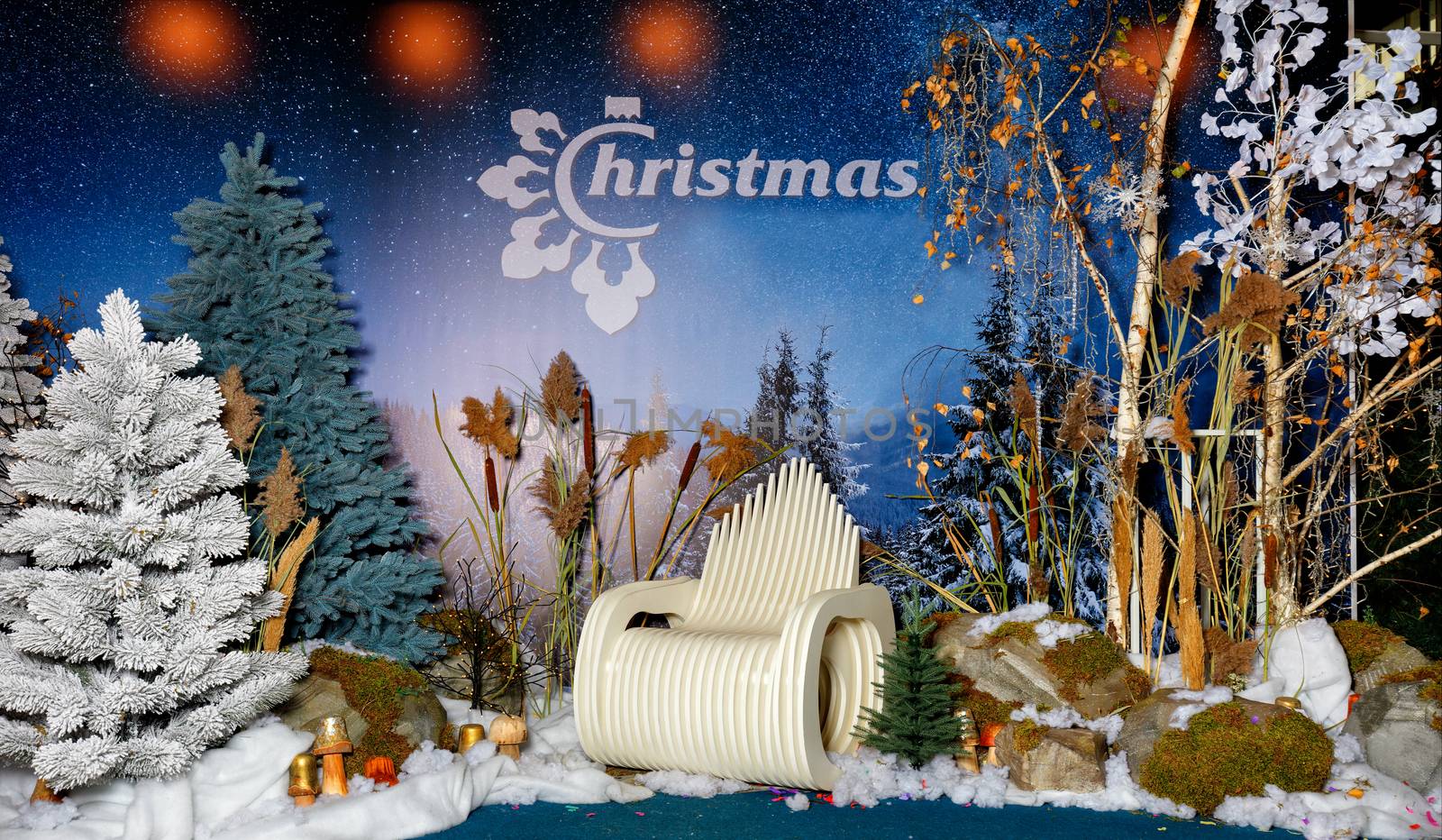 Beautiful panoramic composition of New Year's Eve Christmas evening with artificial trees, snow, boulders and an original wooden chair against the background of the starry evening sky.