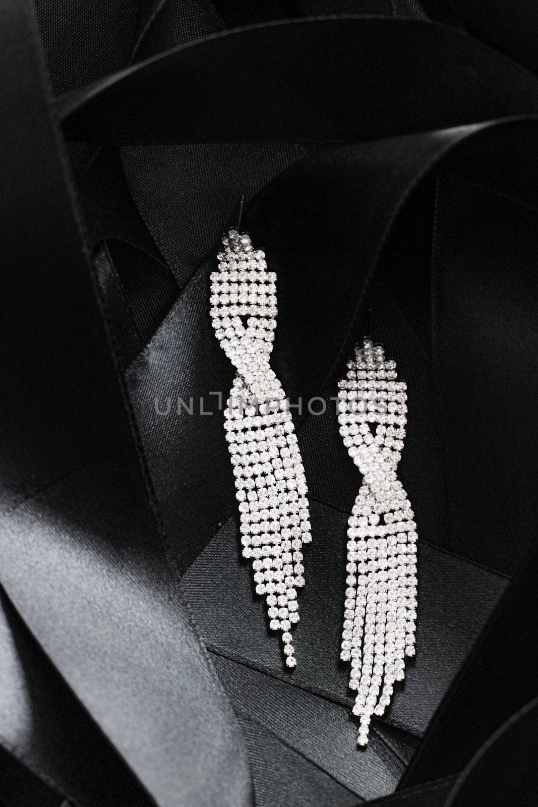 Luxury diamond earrings on black silk ribbon as background, jewelry and fashion brands