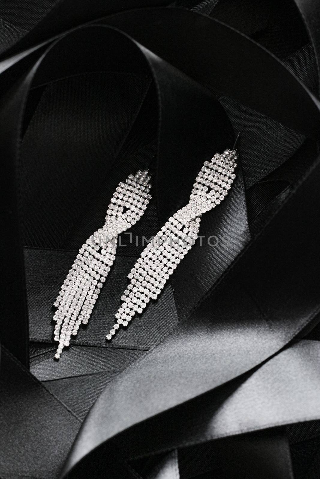 Luxury diamond earrings on black silk ribbon as background, jewelry and fashion brand by Anneleven