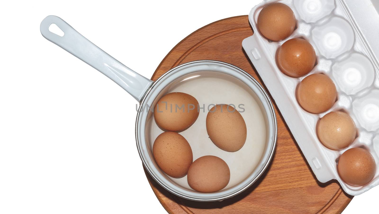 A top close-up shot of a cooking pot and eggs container on a wooden board. Pan is full of water and eggs about to be boiled. Isolated on white background.
