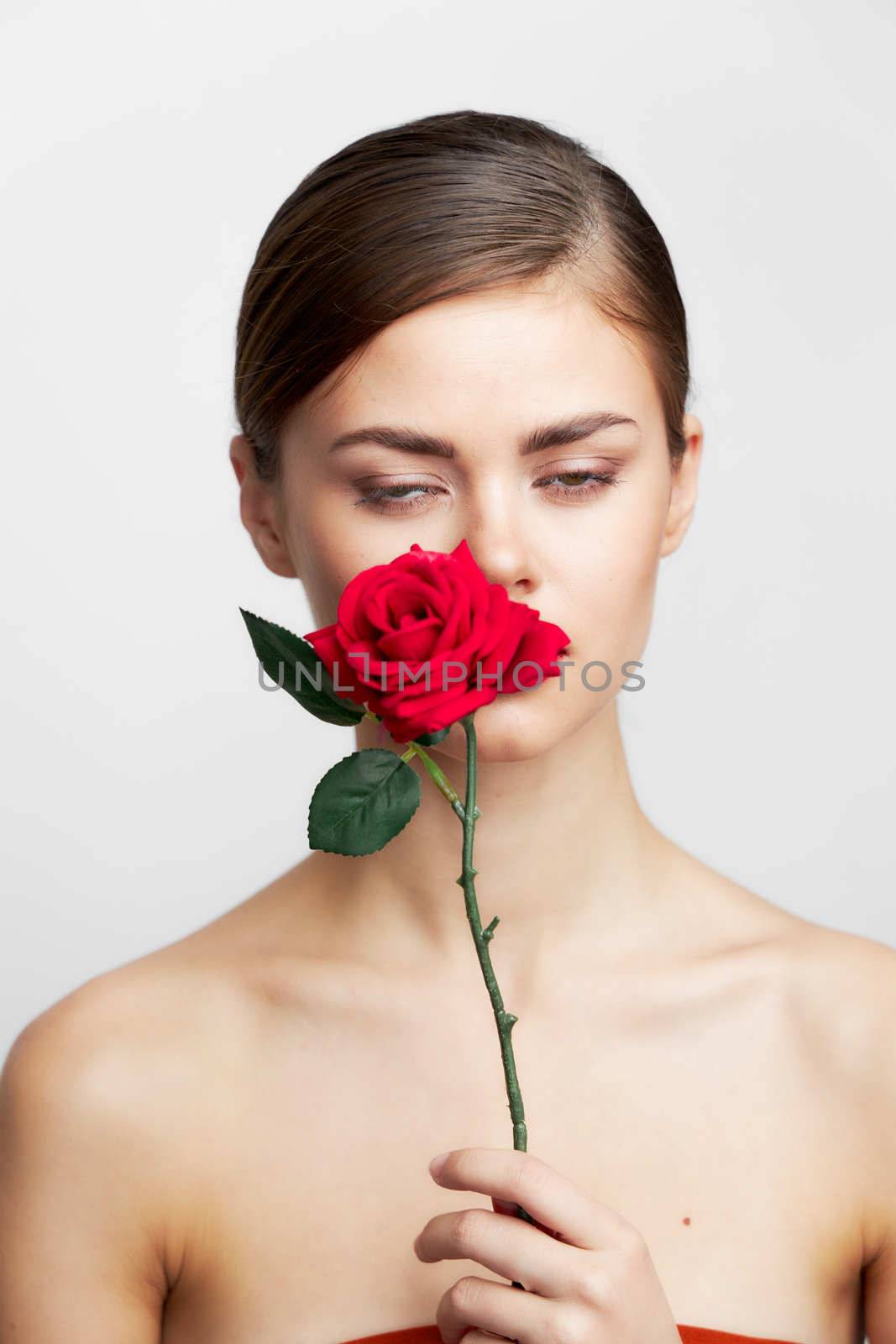 Woman with bare shoulders Holds a flower near her face charm light background