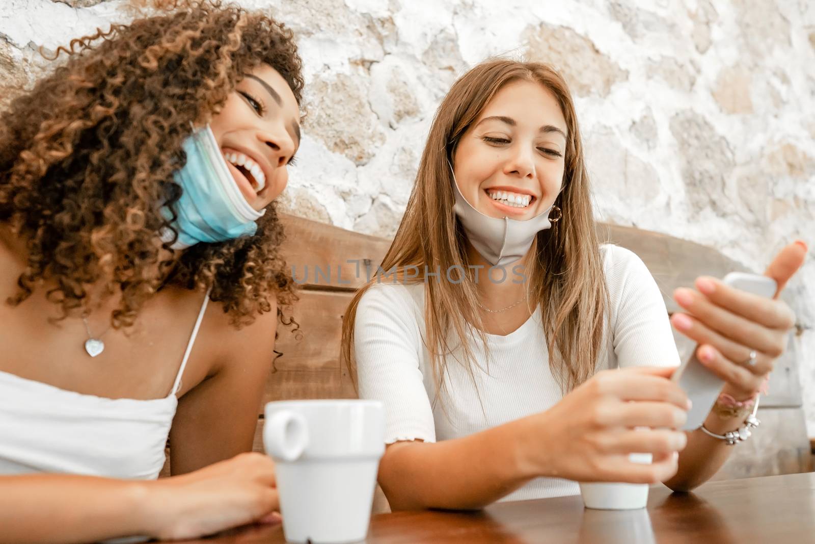 Lifestyle concept, work from home to reinvent your life: two young women, hispanic and caucasian, sitting on a table using a laptop with medical mask protection - New normal job activity by robbyfontanesi