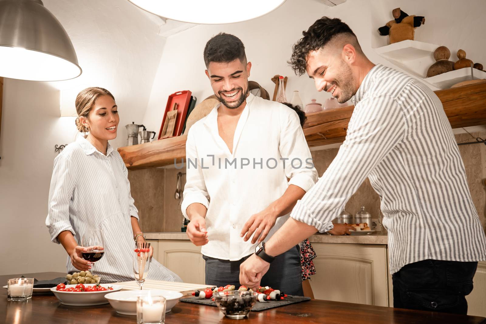 Group of three friends at home preparing savory snacks for the aperitif - Two young man and a young woman smiling in the kitchen waiting for the happy hour by robbyfontanesi