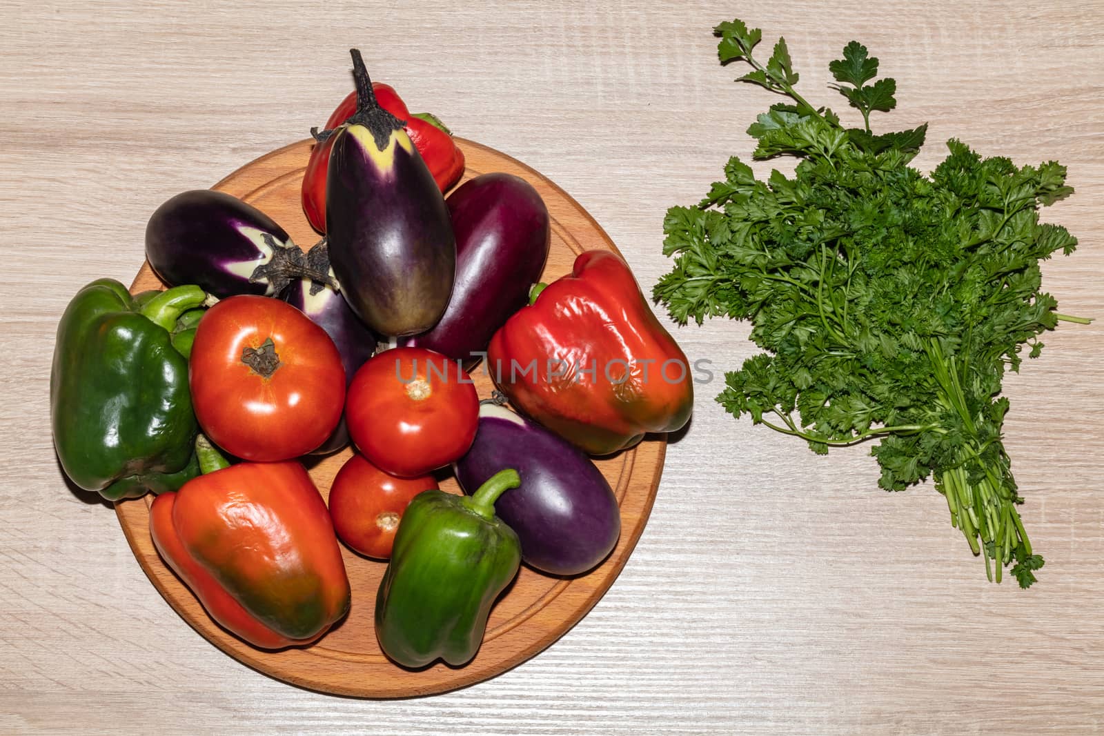 A top close-up shot of various vegetables like tomatoes, parsley, peppers, eggplants lying on a wooden cooking board. Isolated on wooden background.