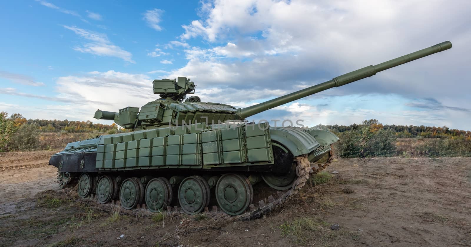 A side shot of russian tank T-64 in the field. Blue cloudy sky as a background.