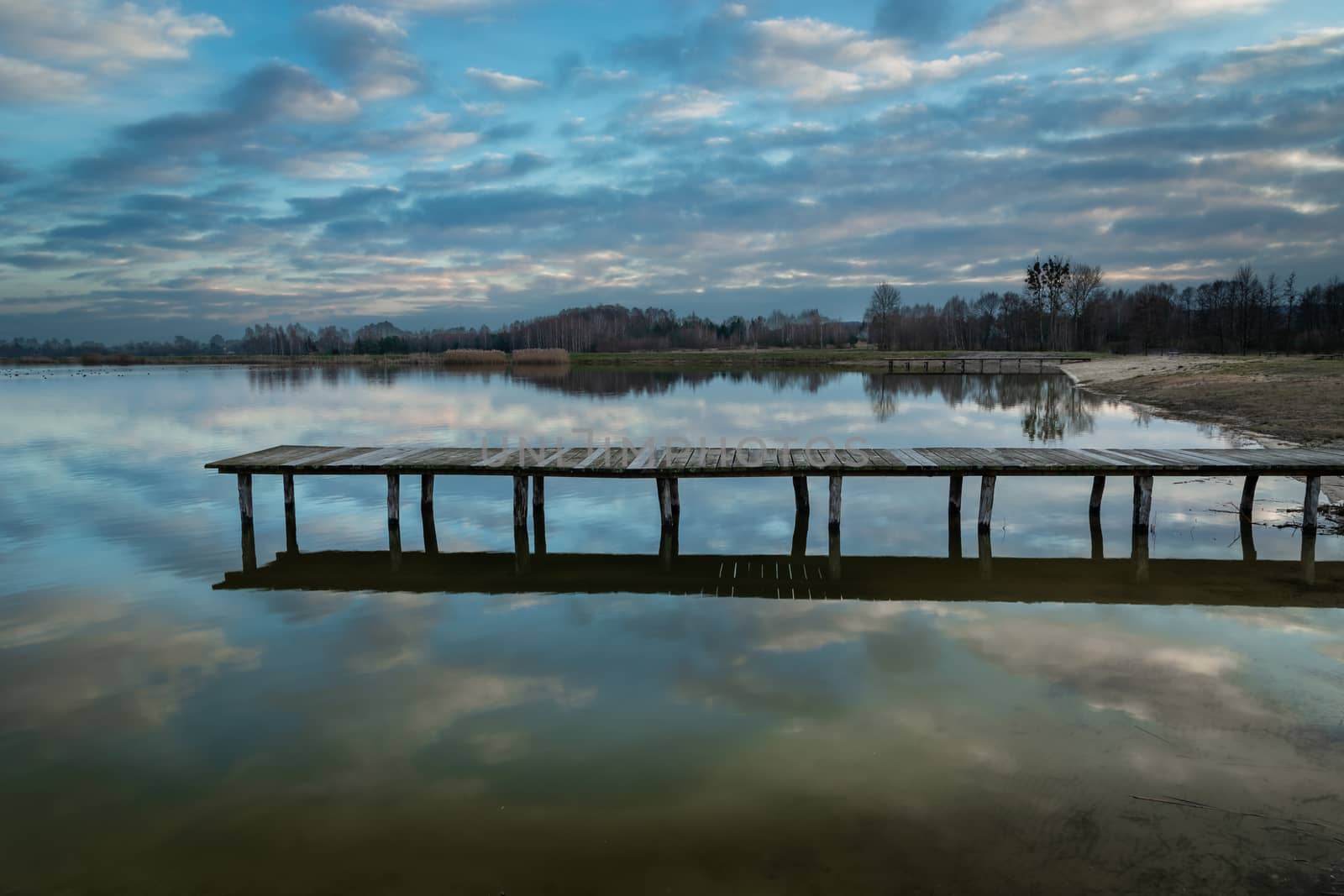 Long wooden bridge on a calm lake and evening clouds