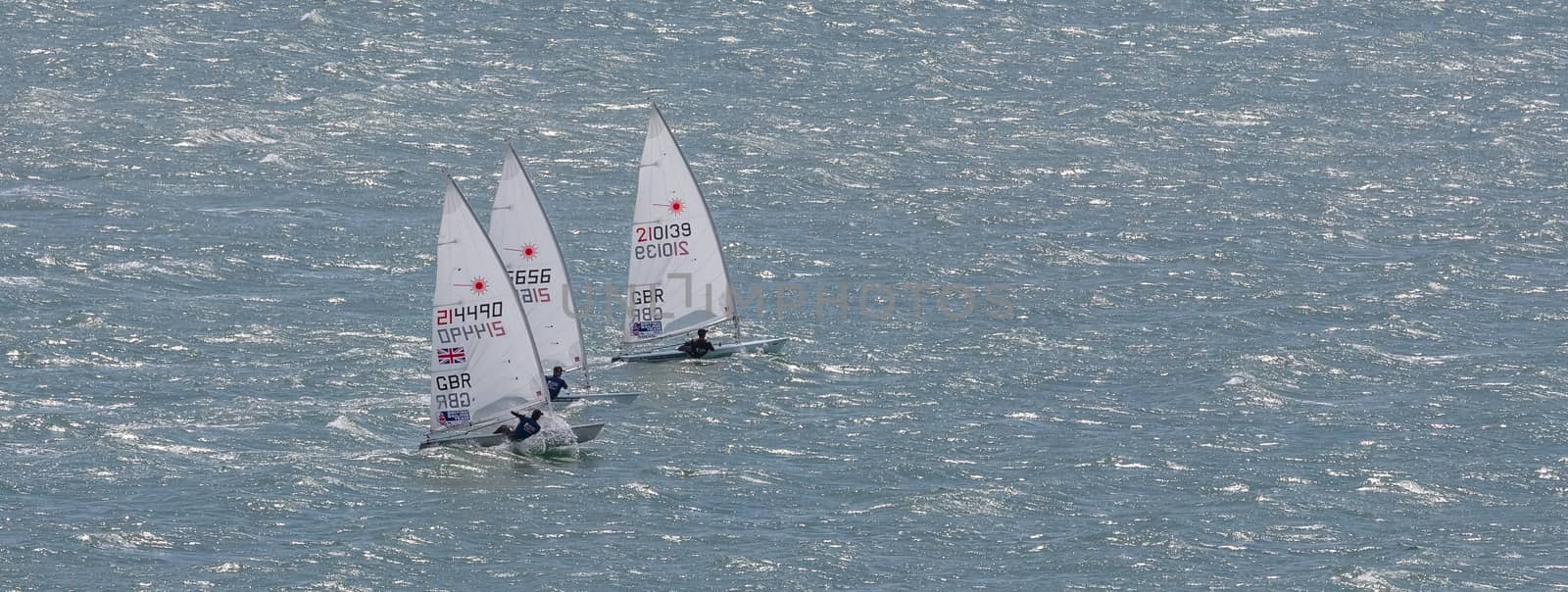 Portland harbour, United Kingdom - July 3, 2020: High Angle aerial panoramic shot of three laser class racing dinghies sailing close to each other in Portland harbour.