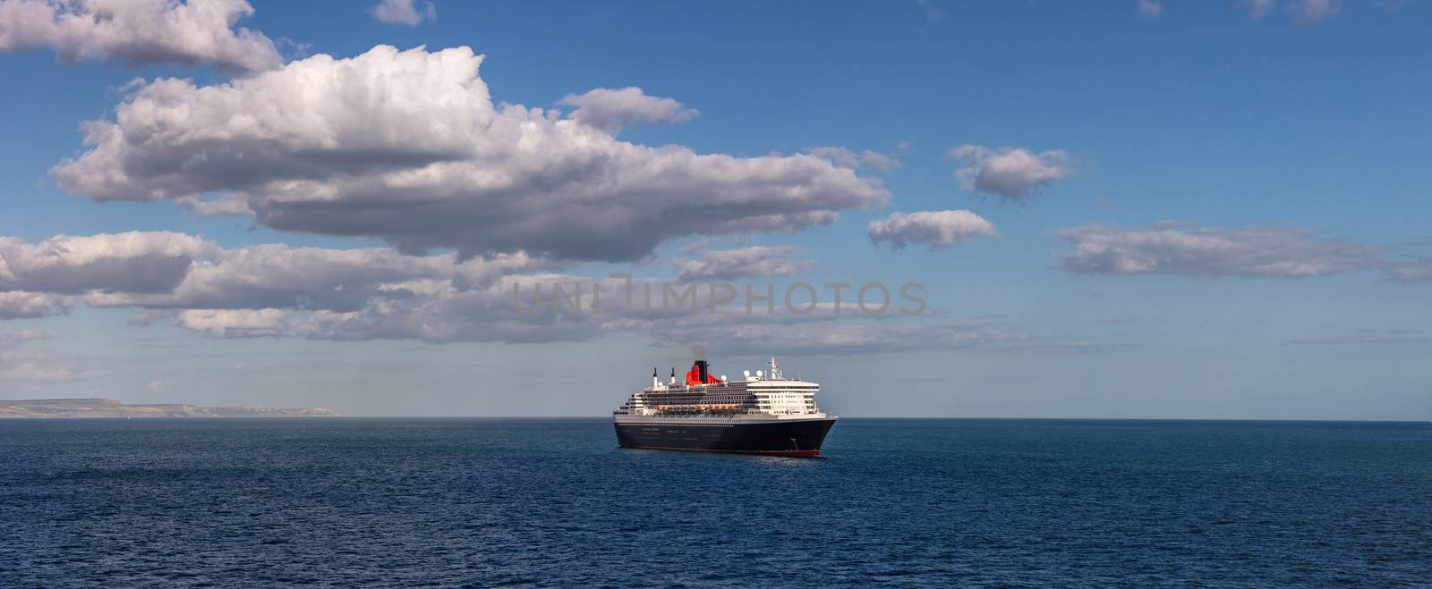 Weymouth Bay, United Kingdom - July 6, 2020: Beautiful panoramic shot of Cunard cruise ship Queen Mary 2 anchored in Weymouth Bay. Beautiful blue sky as a background.
