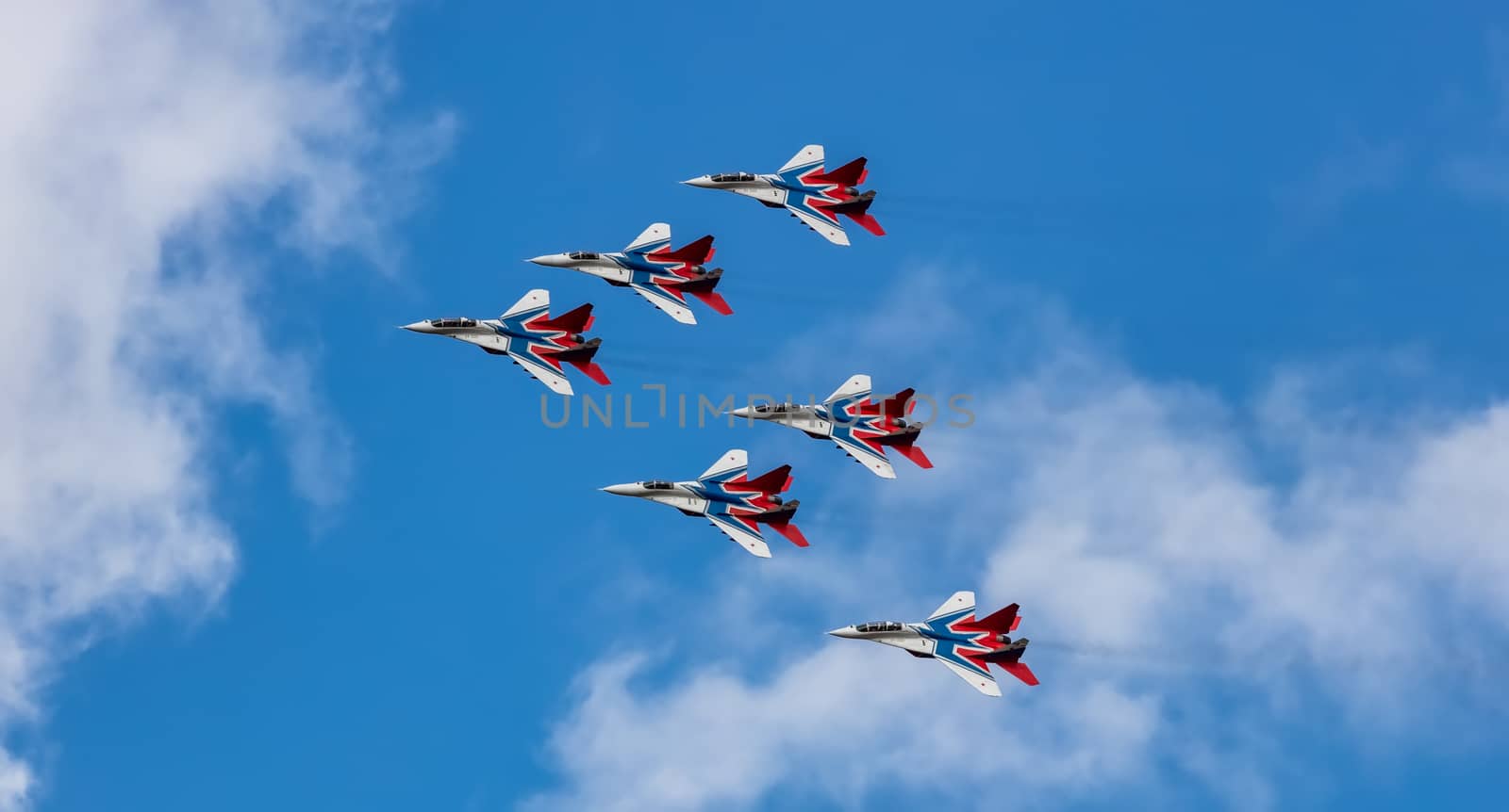 Barnaul, Russia - September 18, 2020: A low angle shot of Strizhi MiG-29 fighter jet squadron performing stunts during an aeroshow. Blue cloudy sky as a background.