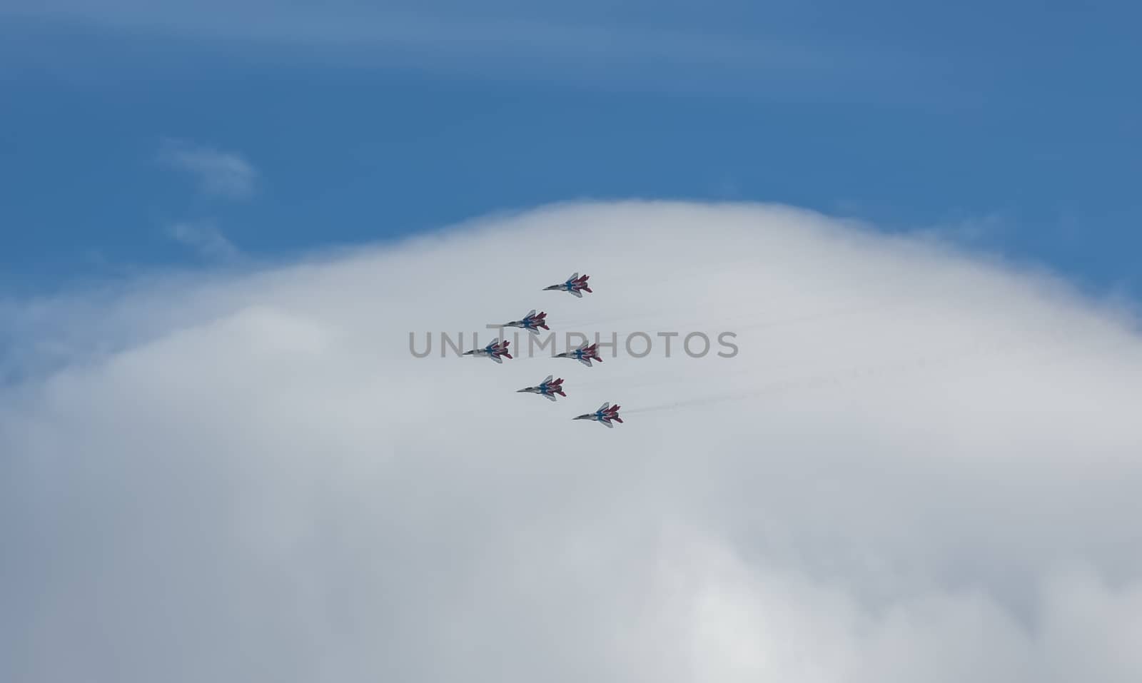 Barnaul, Russia - September 18, 2020: A low angle distant shot of Strizhi MiG-29 fighter jet squadron performing stunts during an aeroshow. Blue cloudy sky as a background.