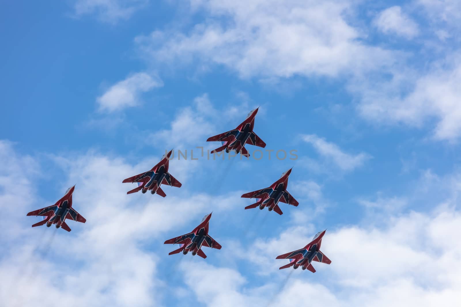 Barnaul, Russia - September 18, 2020: A low angle shot of Strizhi MiG-29 fighter jet squadron performing stunts during an aeroshow. Blue cloudy sky as a background.