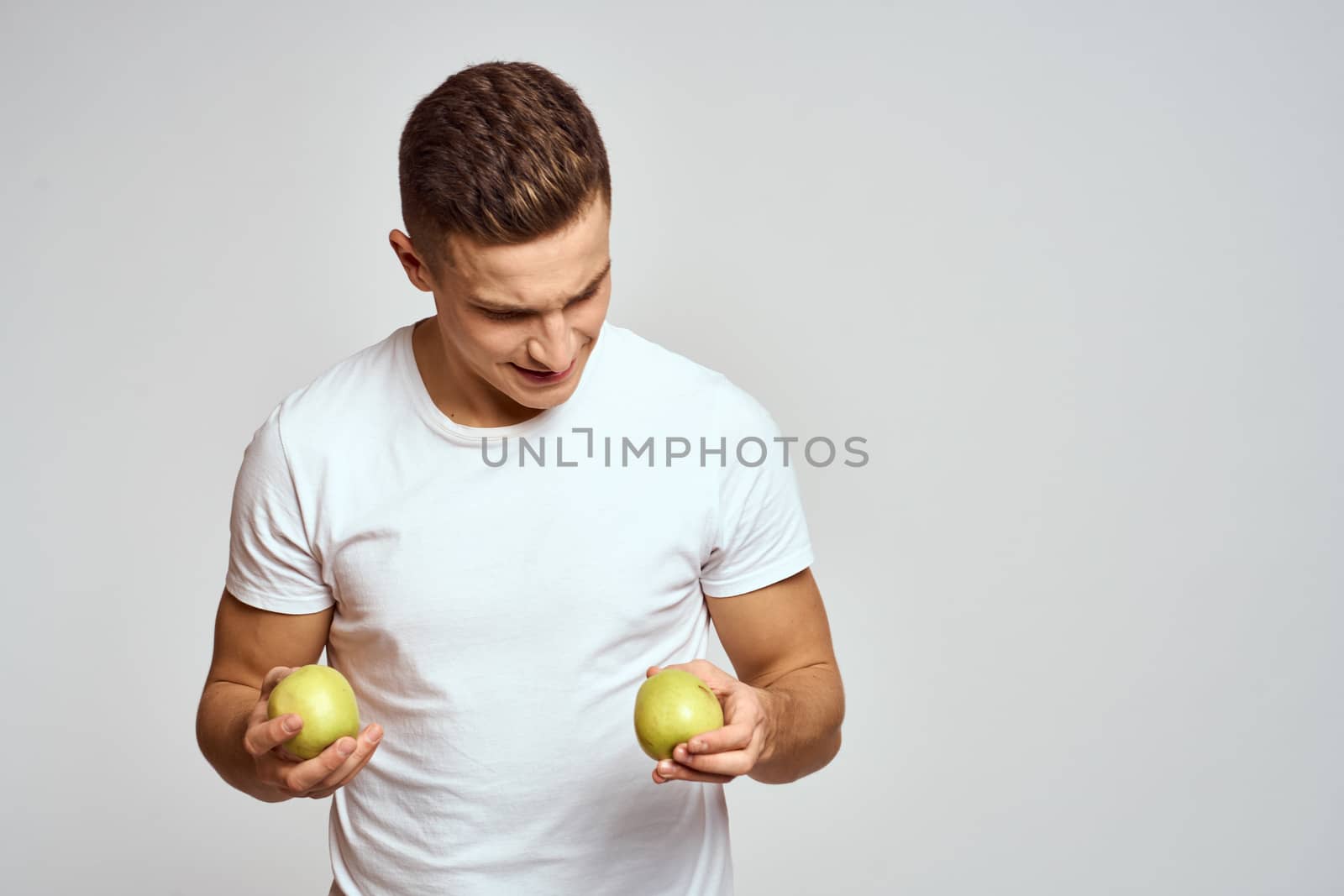 a guy with apples in his hands on a light background in a white t-shirt gesticulate with his hands smile Copy Space Model. High quality photo