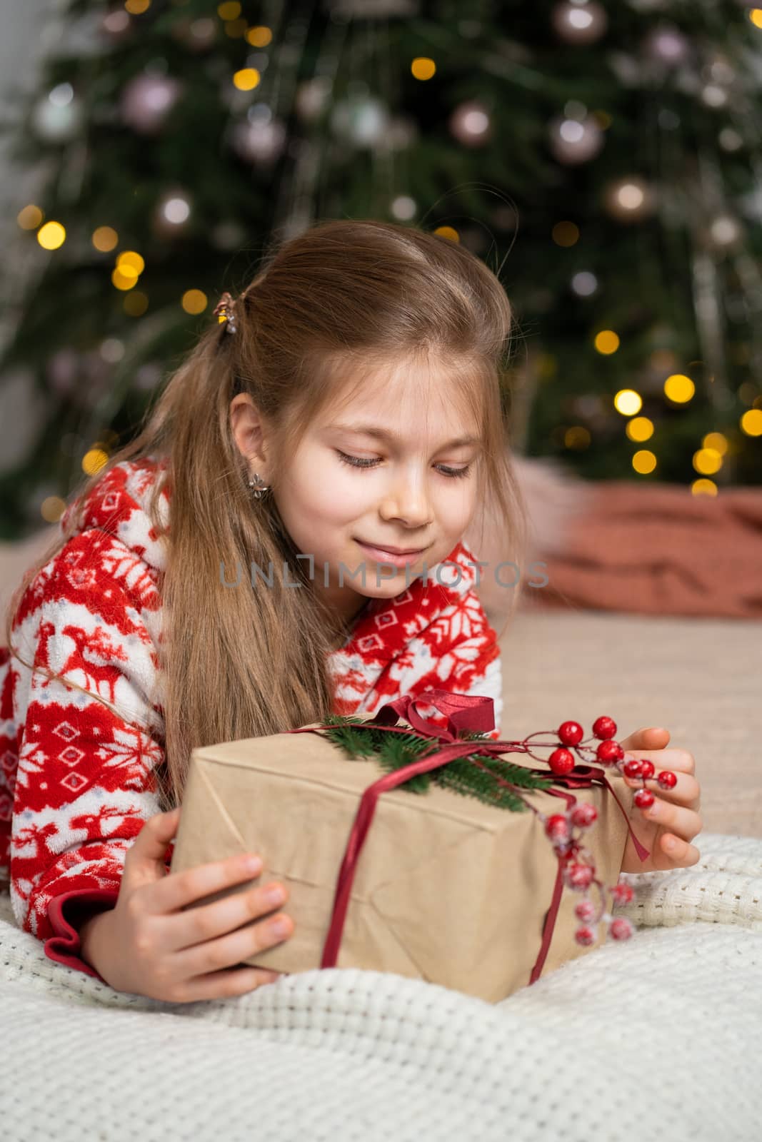 A little girl in pajamas early in the morning found a present from Santa under the tree. Christmas magic fairy tale. Happy childhood.