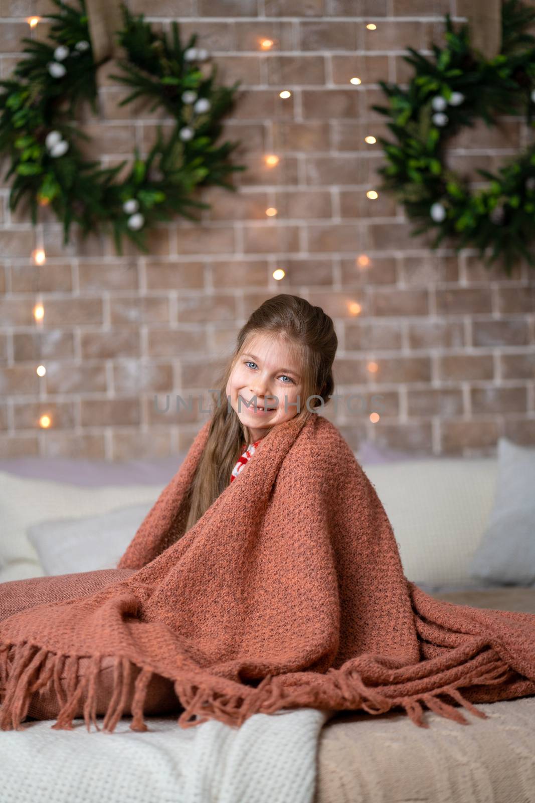 A little girl keeps warm under a cozy knitted blanket.