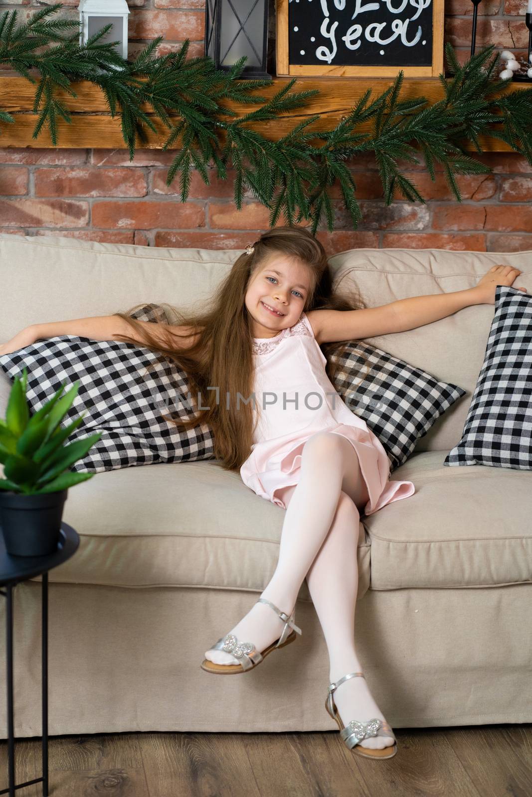 A little girl is sitting on a cozy sofa with checkered pillows.