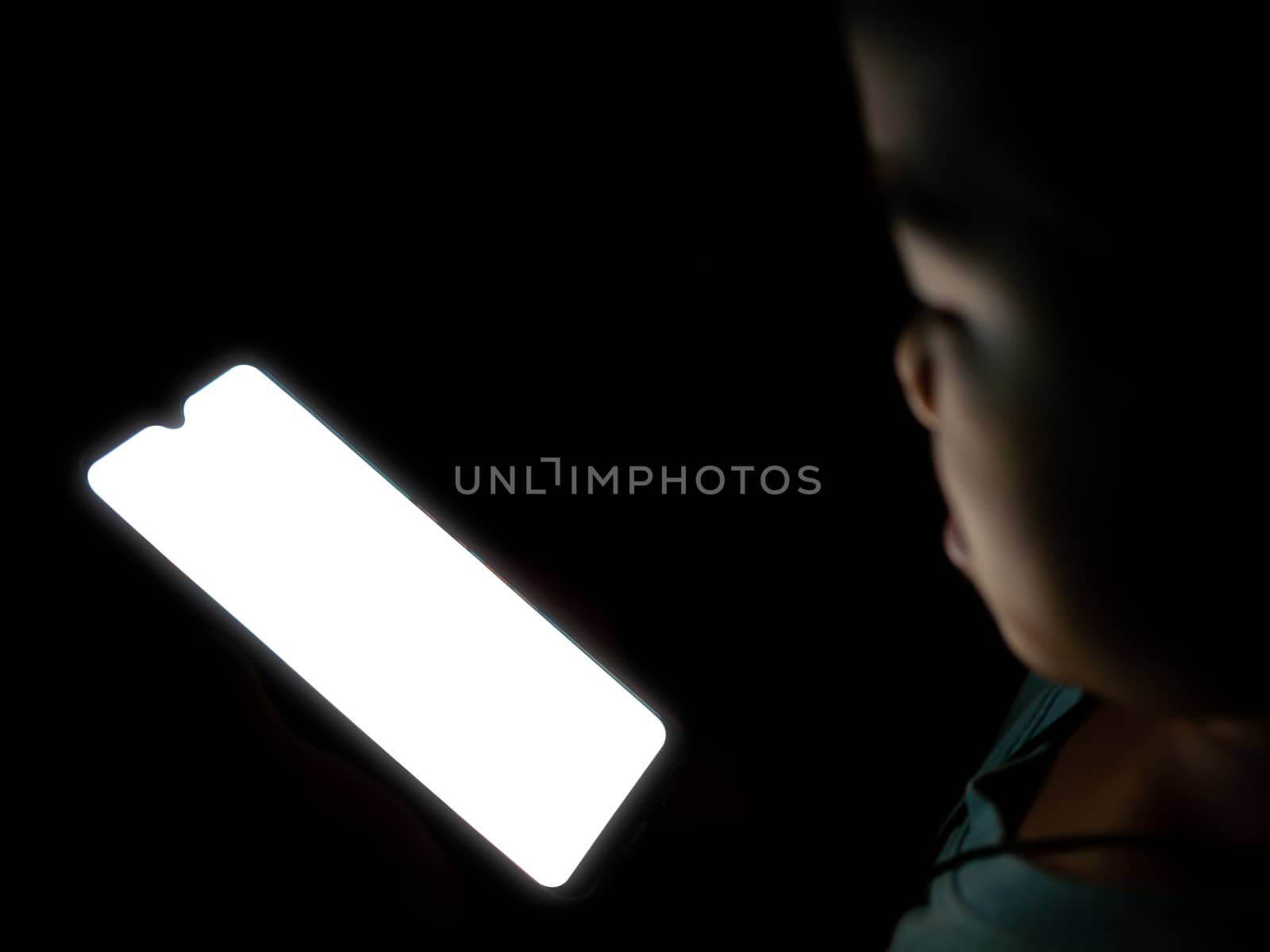 A boy looking at a white blank phone screen on a dark black background.