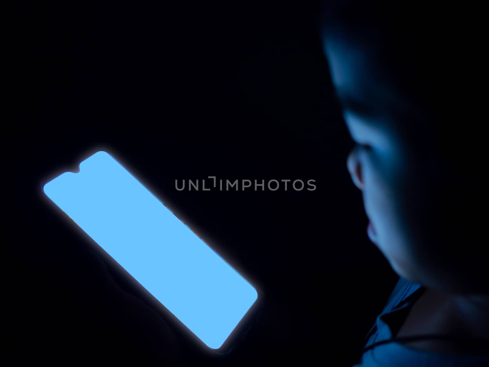 A boy is using a phone with a blank blue screen on a dark black  by Unimages2527