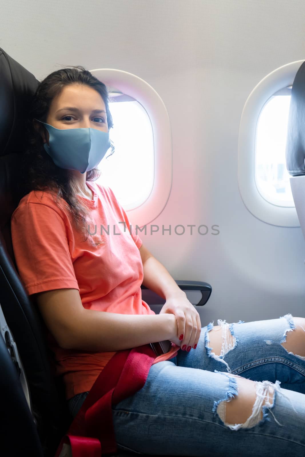 A girl in a medical mask on her face during a flight in the cabin. Air travel during a pandemic.