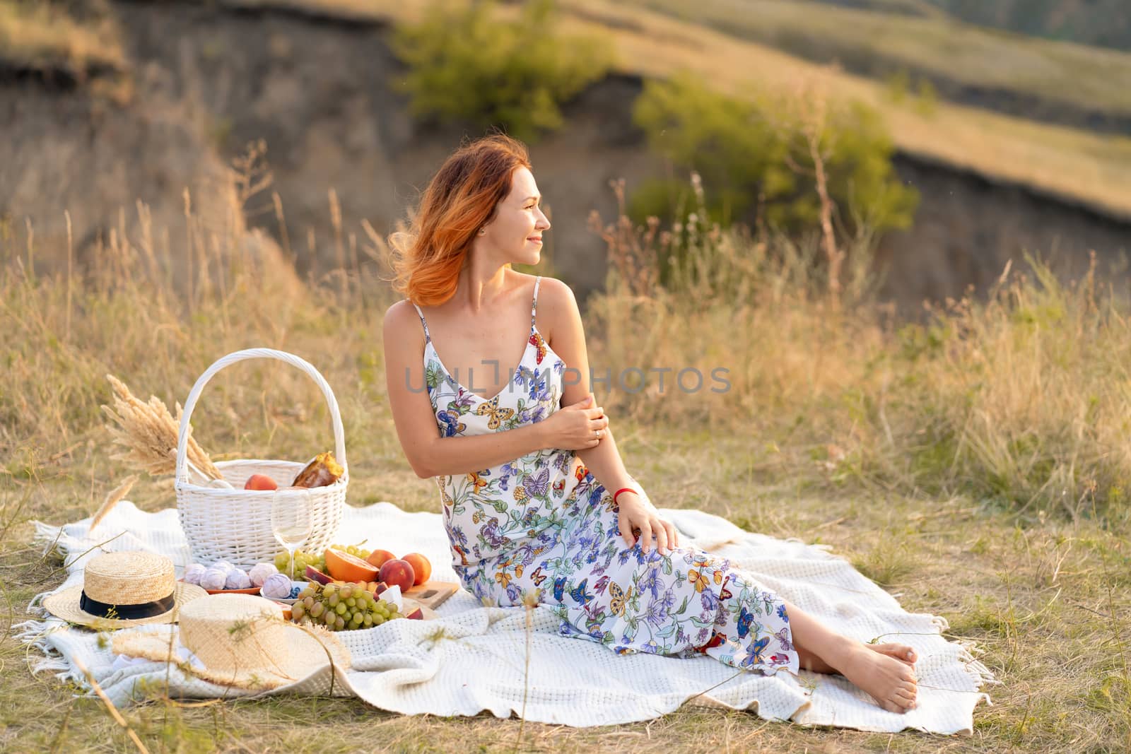 Beautiful red-haired girl enjoys the sunset on the nature. Picnic in the field